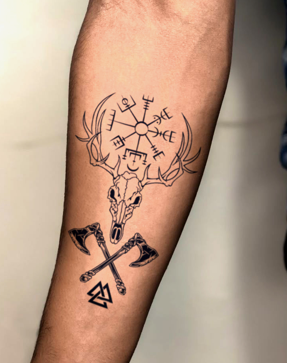 Tattoo of a Viking deer skull with axes and Norse symbols on forearm, showcasing bold ink design.
