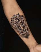 Detailed black tattoo of a sacred winged design on a forearm against a dark background.